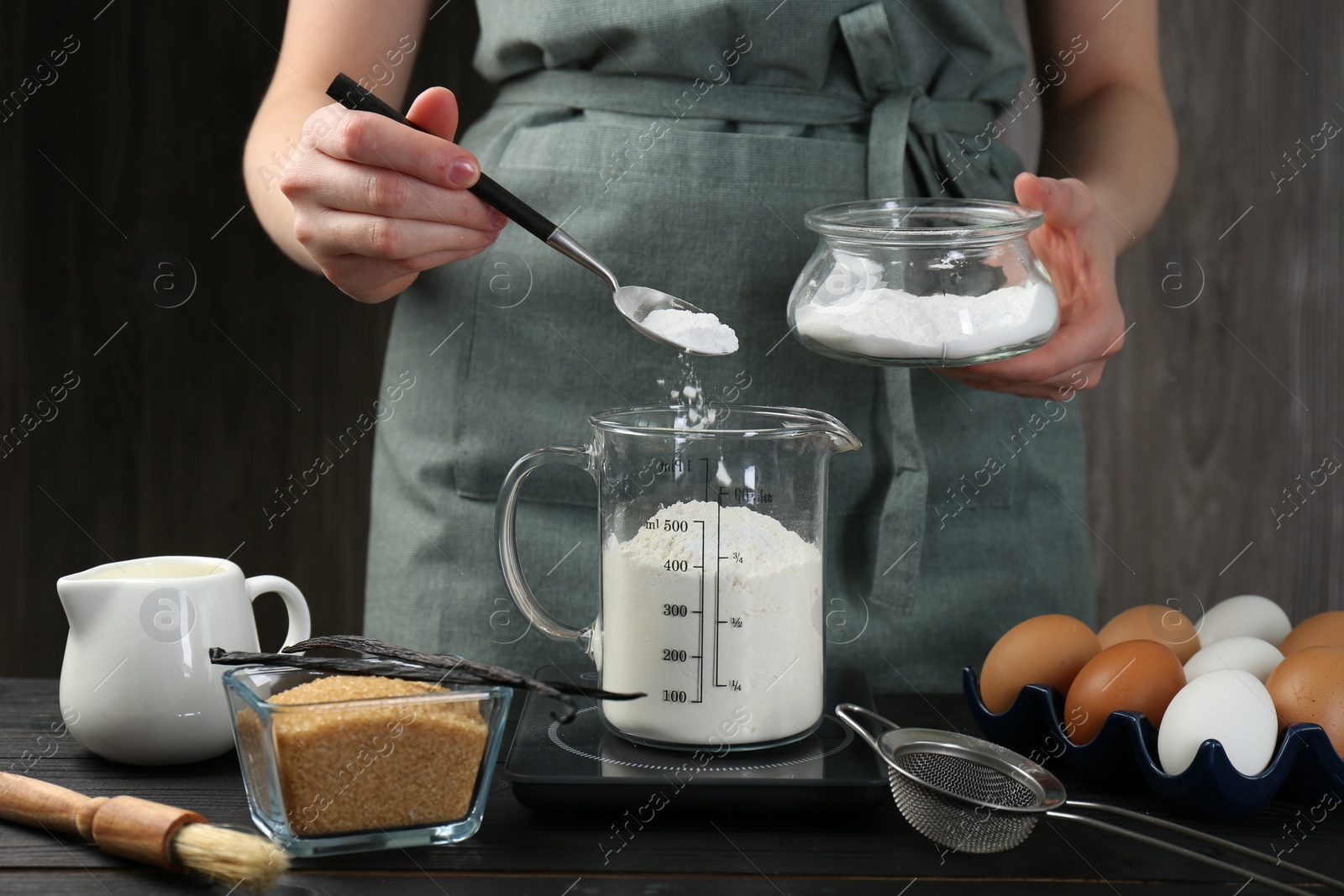 Photo of Woman adding baking powder into measuring cup at black wooden table, closeup