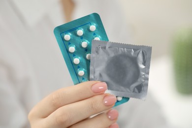 Photo of Woman holding condom and contraceptive pills on blurred background, closeup. Choosing birth control method