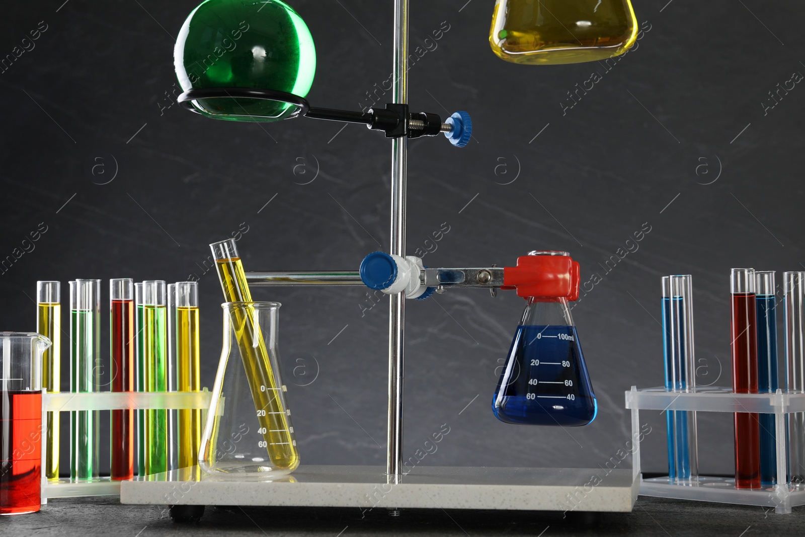 Photo of Retort stand and laboratory glassware with liquids on table against grey background