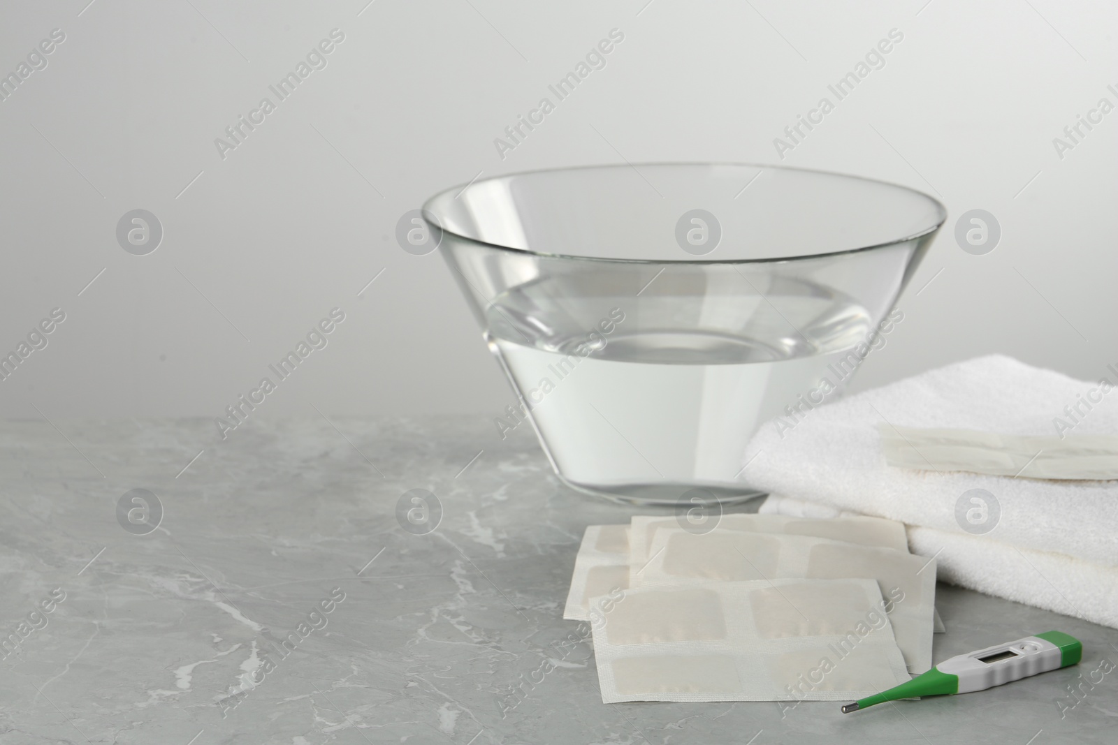 Photo of Mustard plasters, thermometer, towel and bowl with water on light grey marble table, space for text