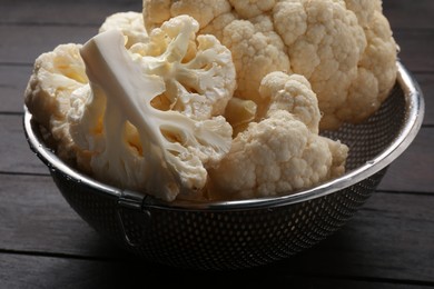Photo of Colander with fresh raw cauliflower on wooden table, closeup