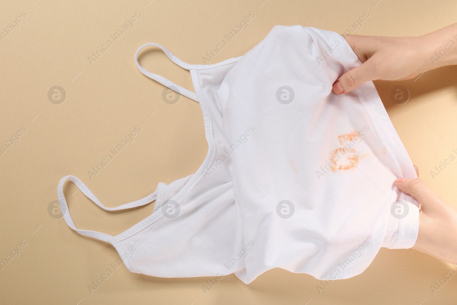 Photo of Woman holding white shirt with yellow stains on beige background, top view