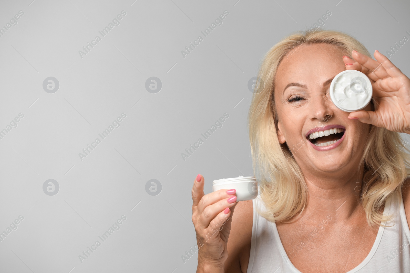 Photo of Portrait of beautiful mature woman with perfect skin holding jars of cream on grey background. Space for text