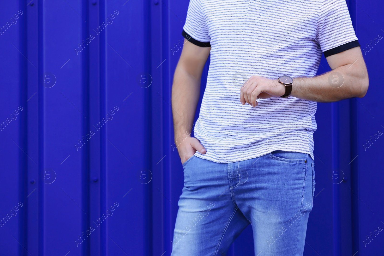 Photo of Young hipster man in stylish jeans posing near color wall
