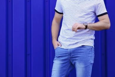 Young hipster man in stylish jeans posing near color wall