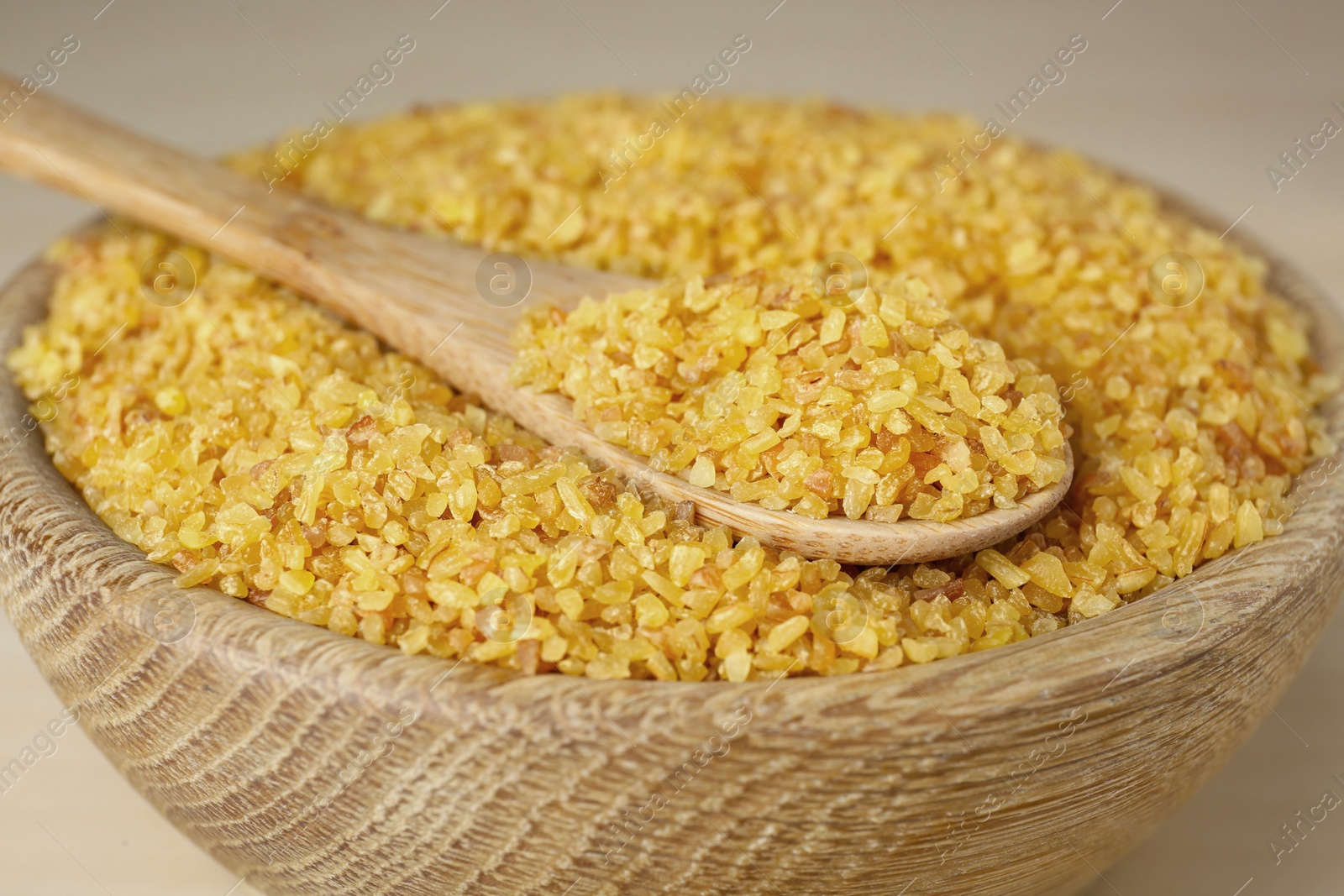 Photo of Bowl and spoon of uncooked bulgur, closeup view