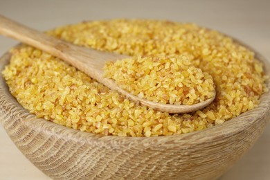 Bowl and spoon of uncooked bulgur, closeup view