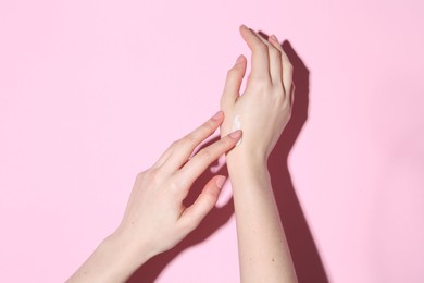 Woman applying cream on her hand against pink background, closeup