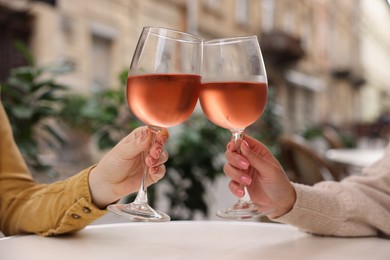 Photo of Women clinking glasses with rose wine at white table in outdoor cafe, closeup