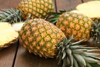 Photo of Whole and cut ripe pineapples on wooden table, closeup