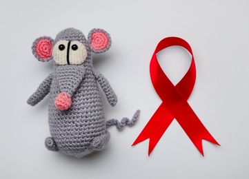 Cute knitted toy mouse and red ribbon on light grey background, flat lay. AIDS disease awareness