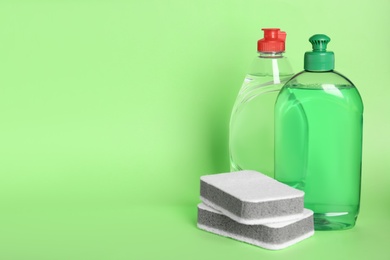 Photo of Detergents and sponges on green background, space for text