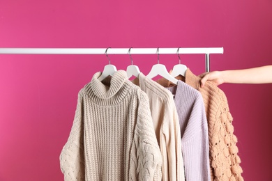 Woman choosing sweater on rack against color background