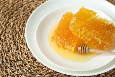 Photo of Natural honeycombs with tasty honey and dipper on wicker mat