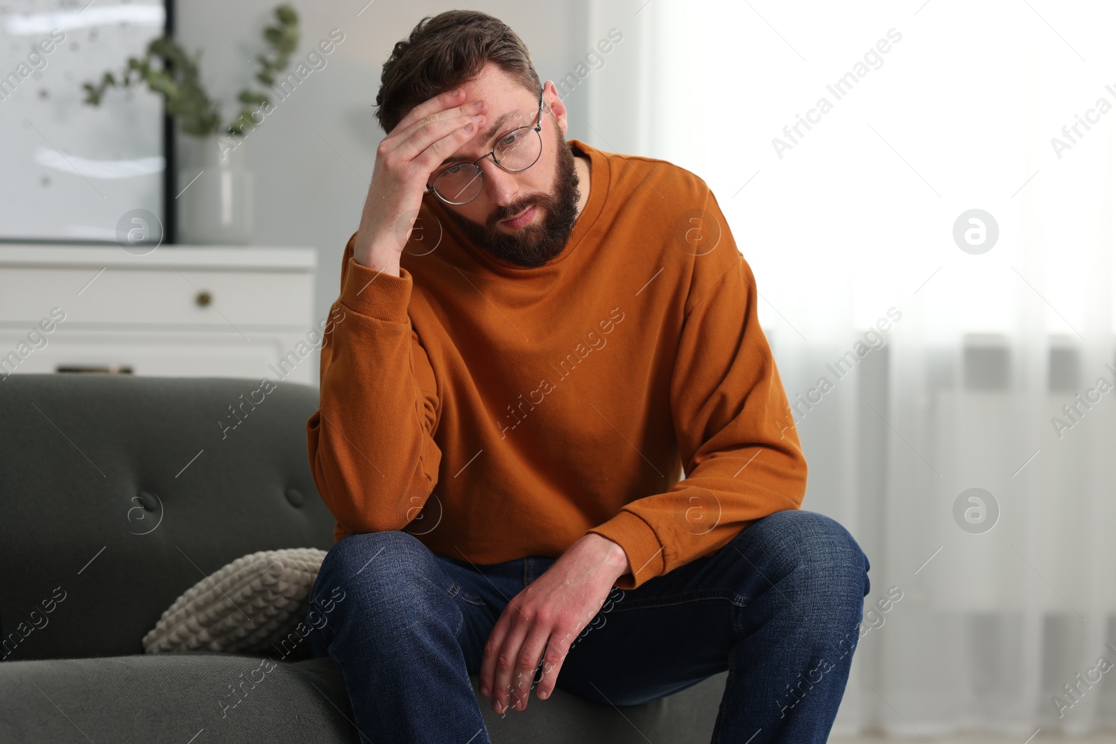 Photo of Overwhelmed man in glasses sitting on sofa at home