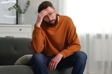 Photo of Overwhelmed man in glasses sitting on sofa at home