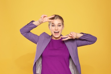 Happy young businesswoman showing victory gesture on color background