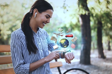 Young woman with modern smartwatch and wireless earphones in park