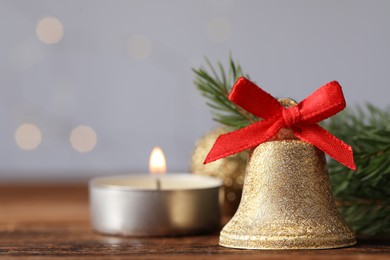 Photo of Bell, fir branches and burning candle on table against blurred background, closeup with space for text. Christmas decor