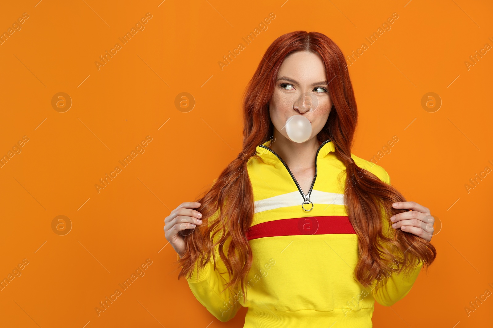 Photo of Portrait of beautiful woman blowing bubble gum on orange background. Space for text