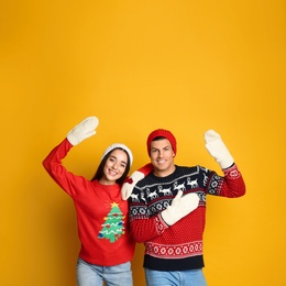 Photo of Couple in Christmas sweaters, knitted mittens and hats on yellow background, space for text