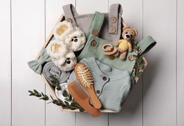 Photo of Children's clothes, shoes, toy bear and pacifier in crate on white wooden table, top view