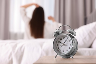 Photo of Alarm clock on nightstand. Woman awakening in bedroom, selective focus