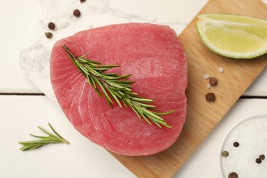 Photo of Raw tuna fillet with rosemary, lime wedge and spices on white wooden table, top view