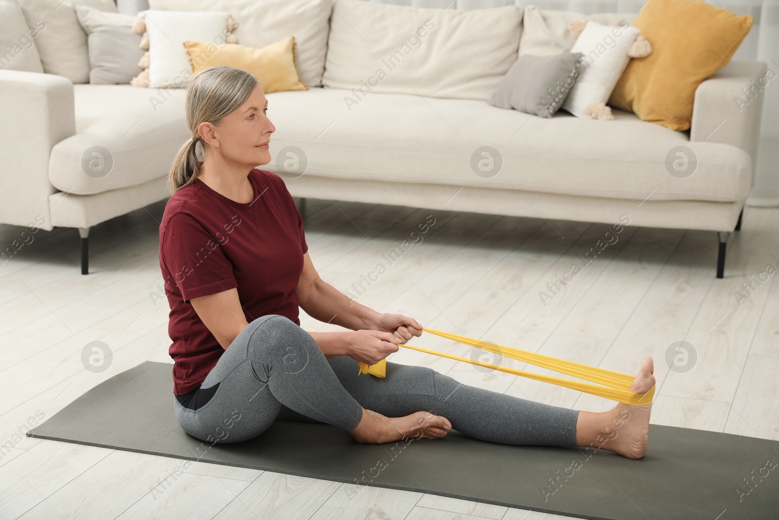 Photo of Senior woman doing exercise with fitness elastic band on mat at home