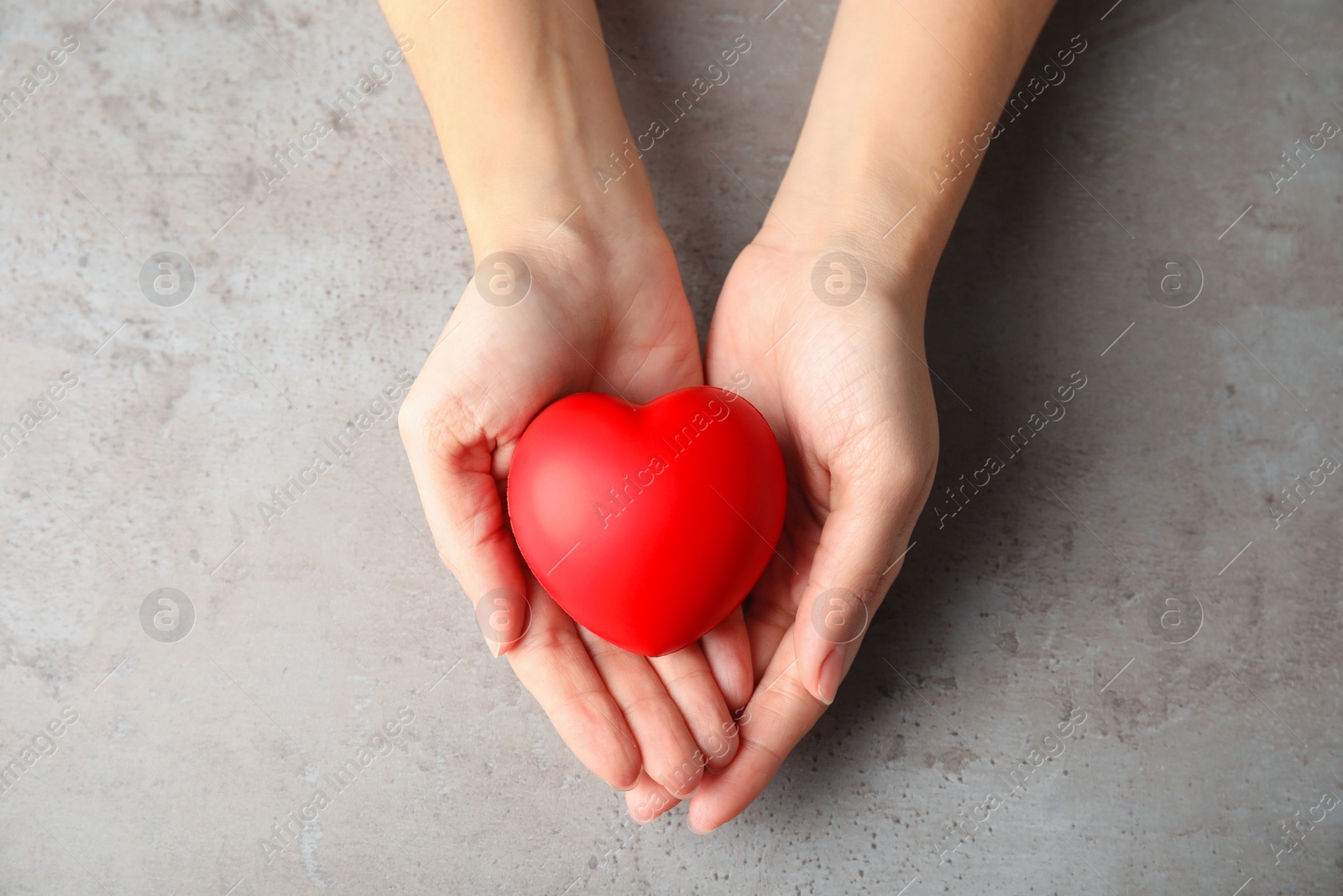 Photo of Woman holding red heart on gray table, top view. Cardiology concept