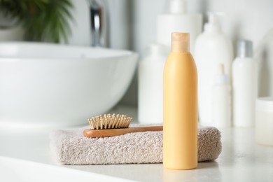 Photo of Bottle of shampoo, towel and wooden hairbrush near sink on bathroom counter, space for text