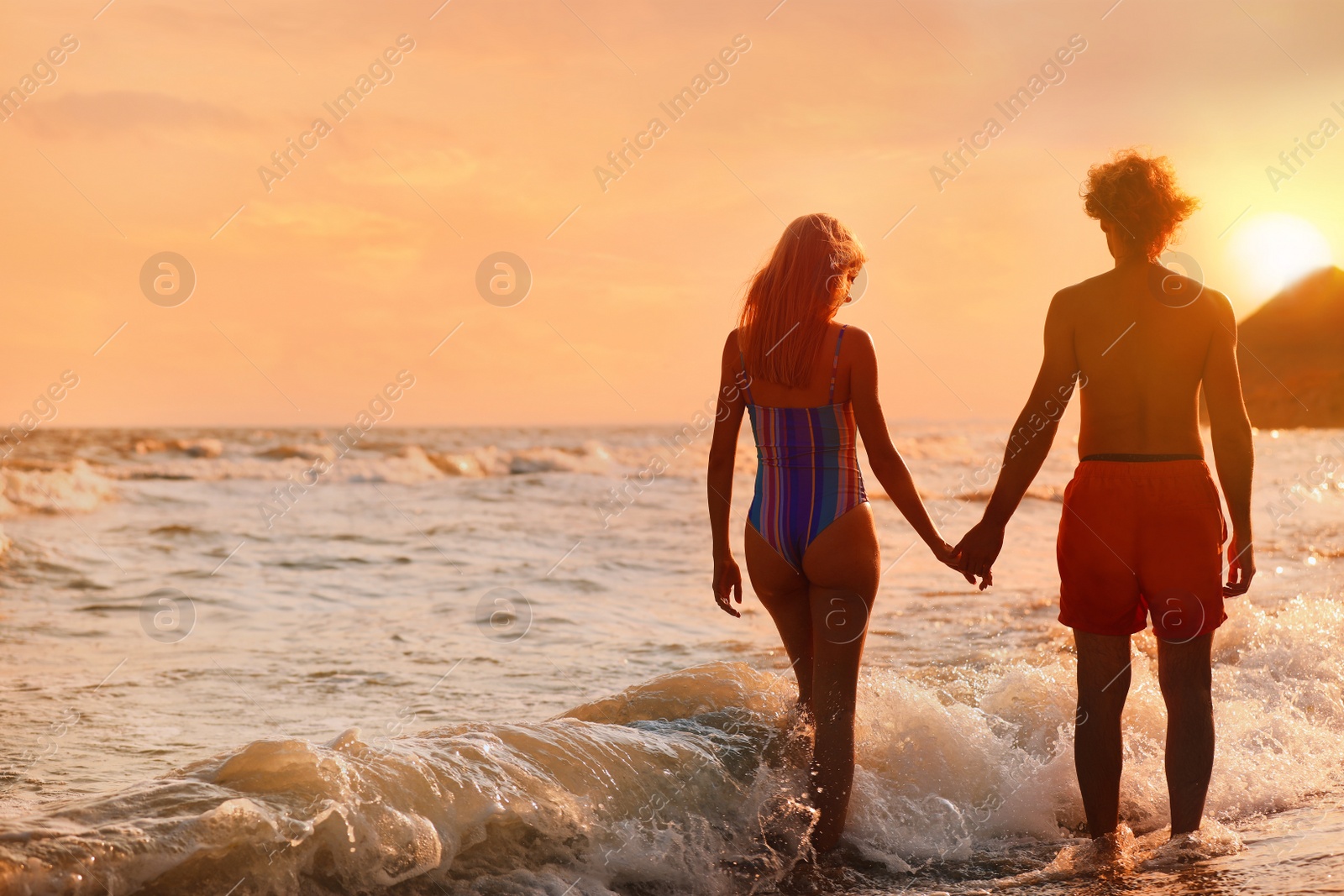 Photo of Young woman in bikini and her boyfriend on beach at sunset. Lovely couple