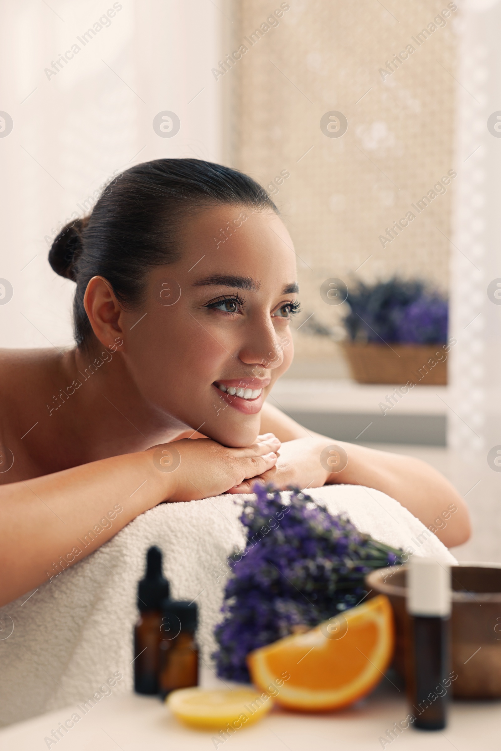 Photo of Beautiful young woman relaxing on massage couch and bottles of essential oil with ingredients on table in spa salon