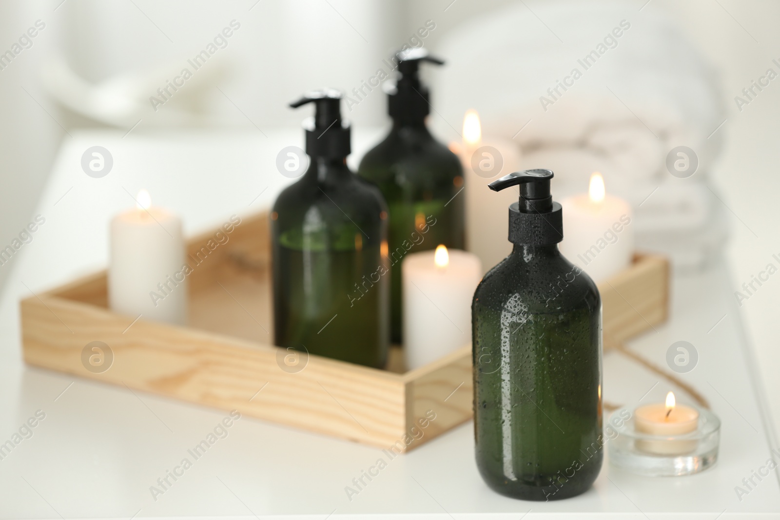 Photo of Wooden tray with soap dispensers and burning candles on white table