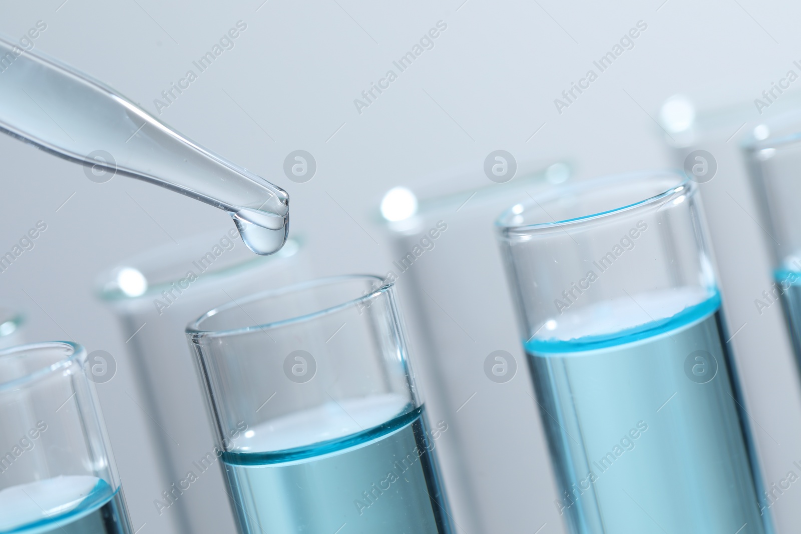 Photo of Dripping liquid from pipette into test tube on light background, closeup