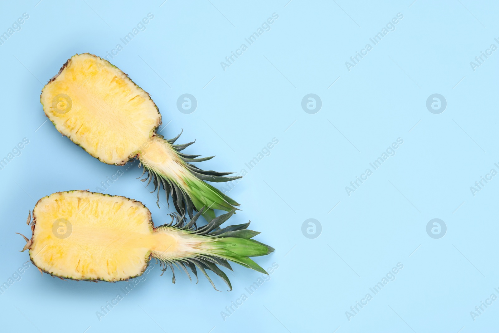 Photo of Halves of ripe pineapple on light blue background, flat lay. Space for text