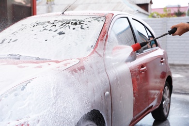 Photo of Man foaming red auto at car wash. Cleaning service