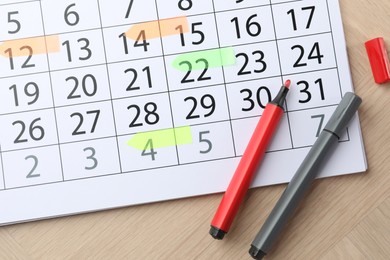 Photo of Timetable. Calendar page with marked dates and felt pens on wooden table, top view