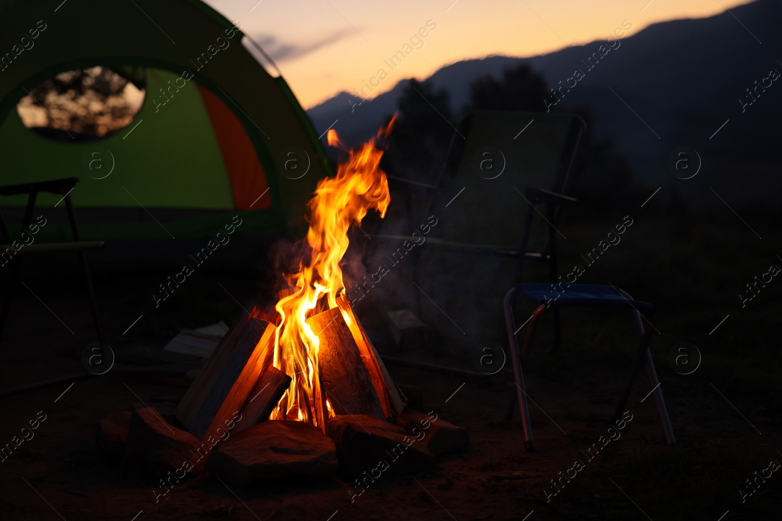 Photo of Beautiful bonfire and folding chairs near camping tent outdoors in evening