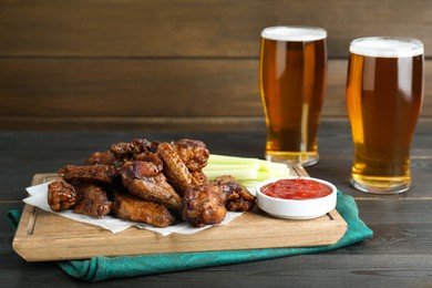 Photo of Delicious chicken wings served with beer on black wooden table