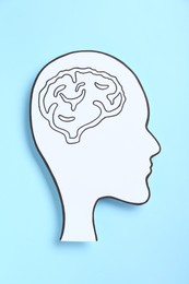 Paper human head cutout with drawing of brain on light blue background, top view