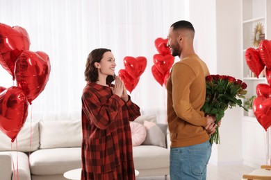 Photo of Man hiding bouquet of red roses for his beloved woman at home. Valentine's day celebration