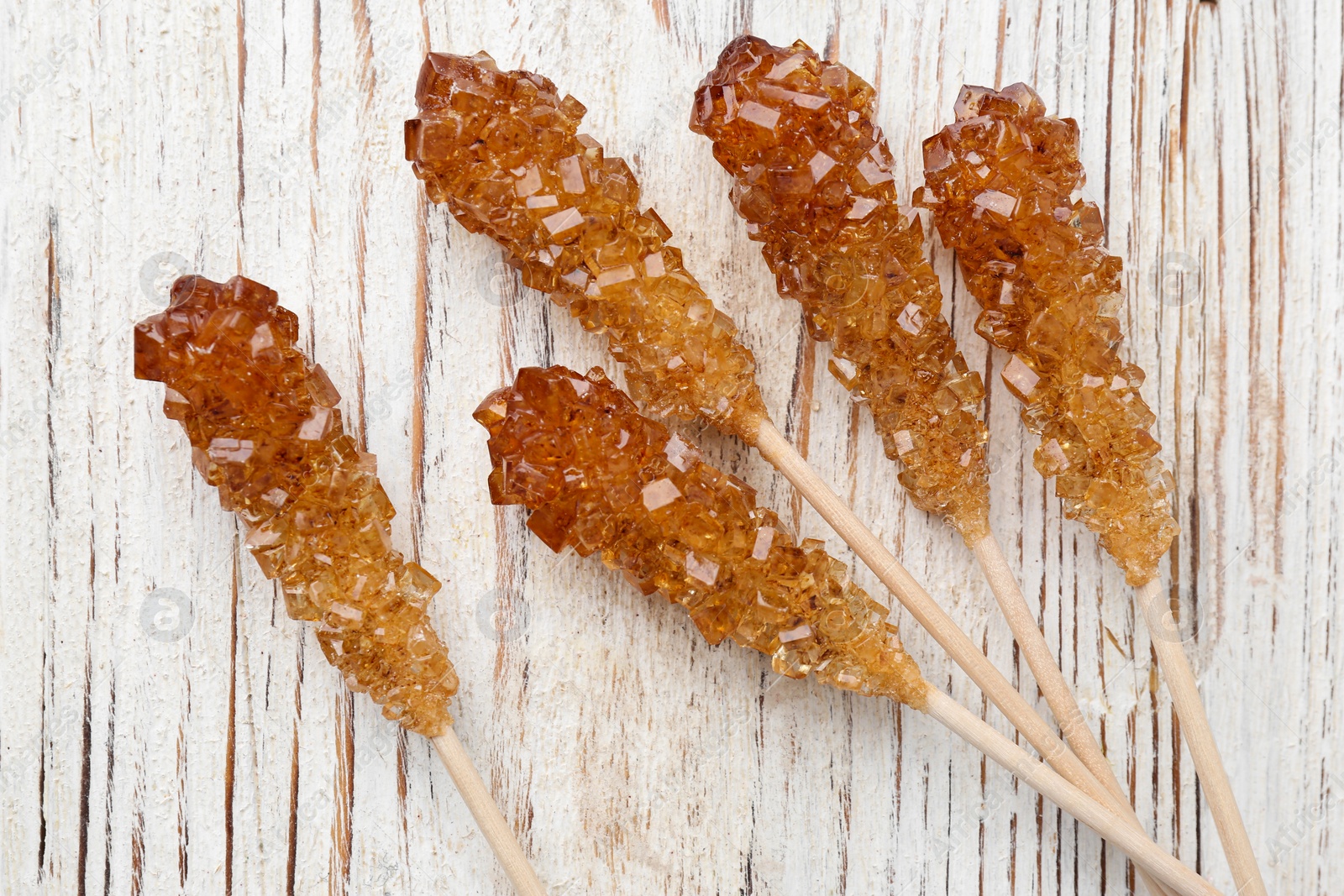 Photo of Sticks with sugar crystals on white wooden table, flat lay. Tasty rock candies