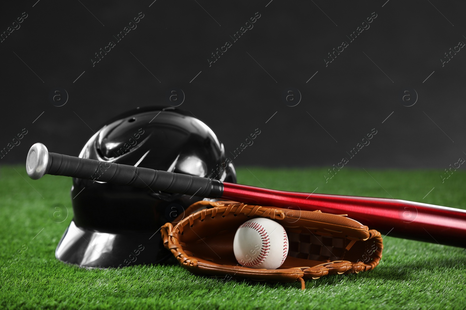 Photo of Baseball bat, batting helmet, leather glove and ball on green grass against dark background. Space for text