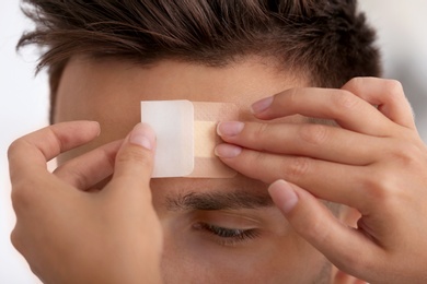 Photo of Woman applying adhesive bandage on man's forehead, closeup view