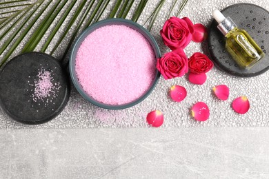 Natural sea salt in bowl, spa stones, cosmetic product, rose flowers and petals on grey table, flat lay. Space for text