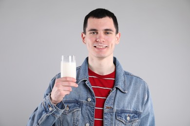 Photo of Happy man with milk mustache holding glass of tasty dairy drink on gray background