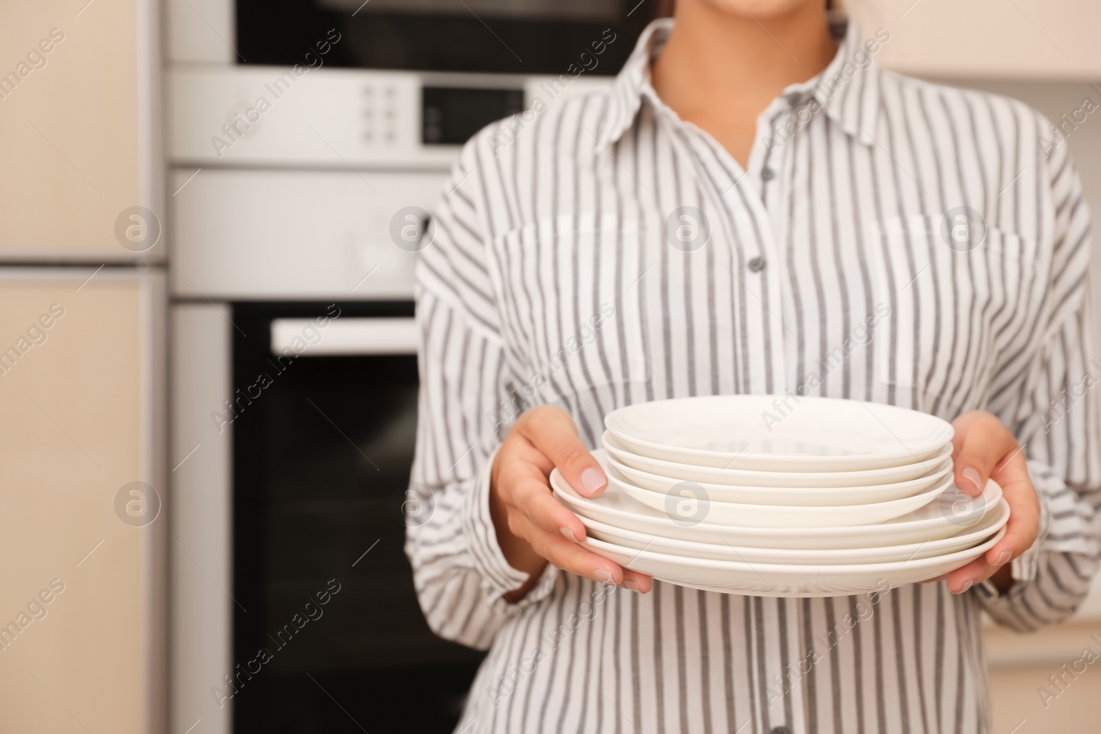 Photo of Woman holding stack of clean dishes in kitchen, closeup