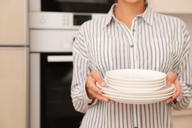 Photo of Woman holding stack of clean dishes in kitchen, closeup
