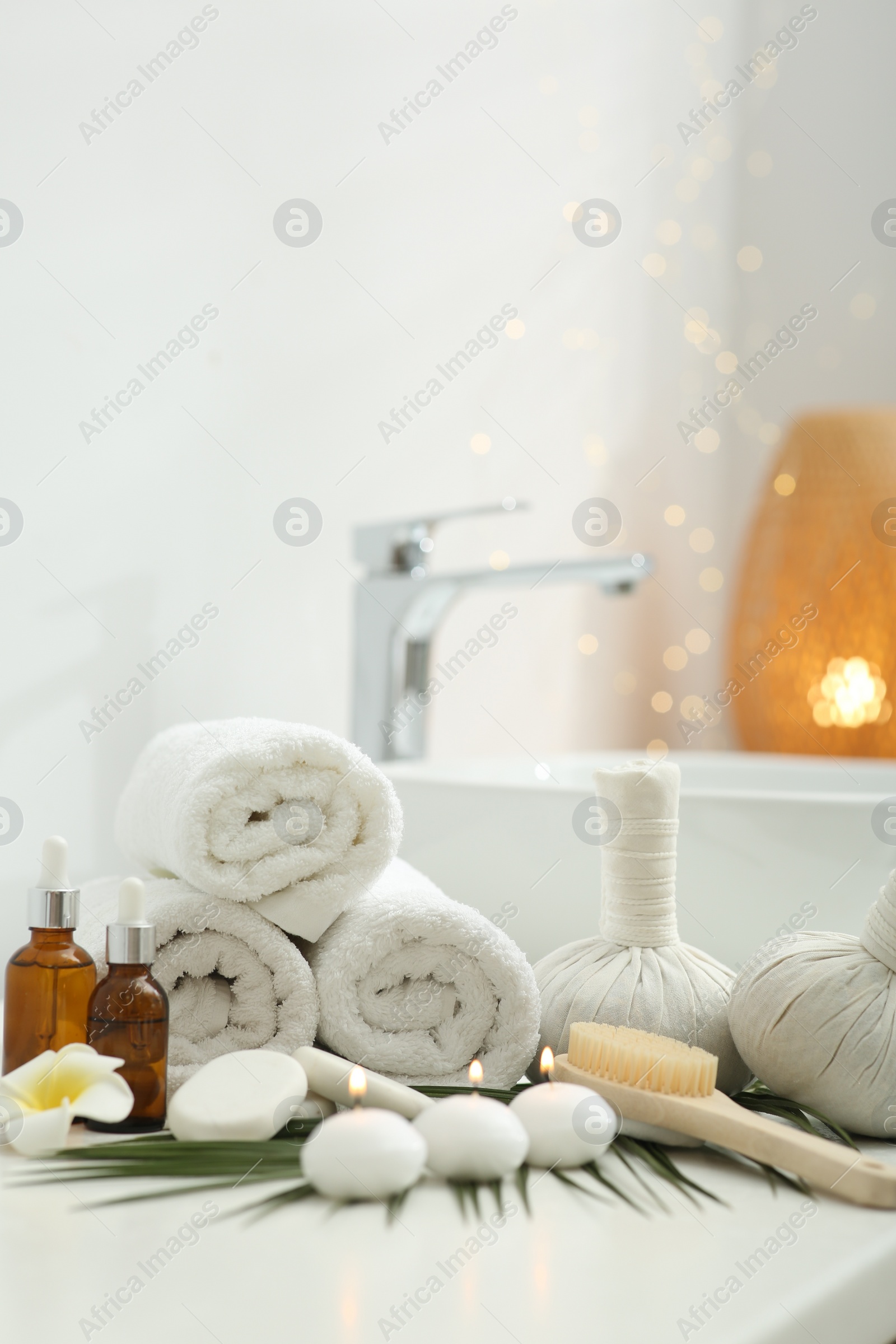 Photo of Spa composition. Rolled towels, herbal bags, cosmetic products and burning candles on white countertop in bathroom